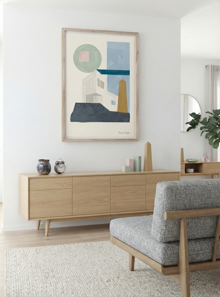 A framed  Geometric Art Poster inspired by Bauhaus architecture with neutral tones, sage green and blue accents, from an original acrylic painting by Francis Phylae.hangs on a white wall above a light wood sideboard in a bright, modern living room. The print features shapes and architectural forms in muted blue, green, beige, and yellow tones.