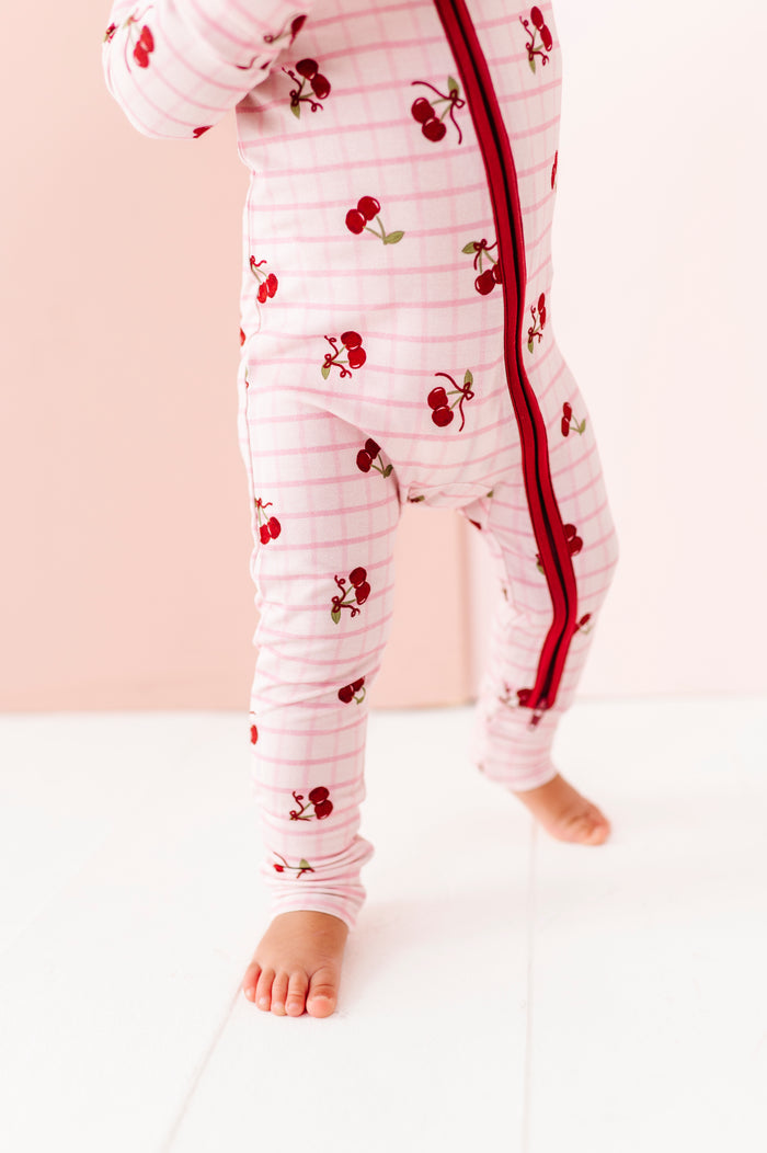 Baby wearing a white onesie with red cherry pattern on a light pink background