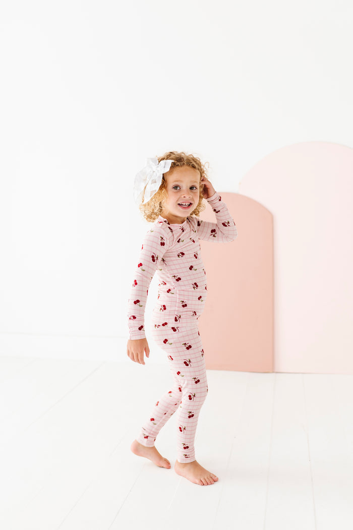 Child wearing a cherry-patterned onesie on a white background