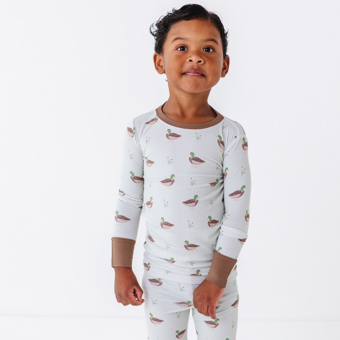 Child wearing a white long-sleeve shirt and pants with duck pattern on a white background