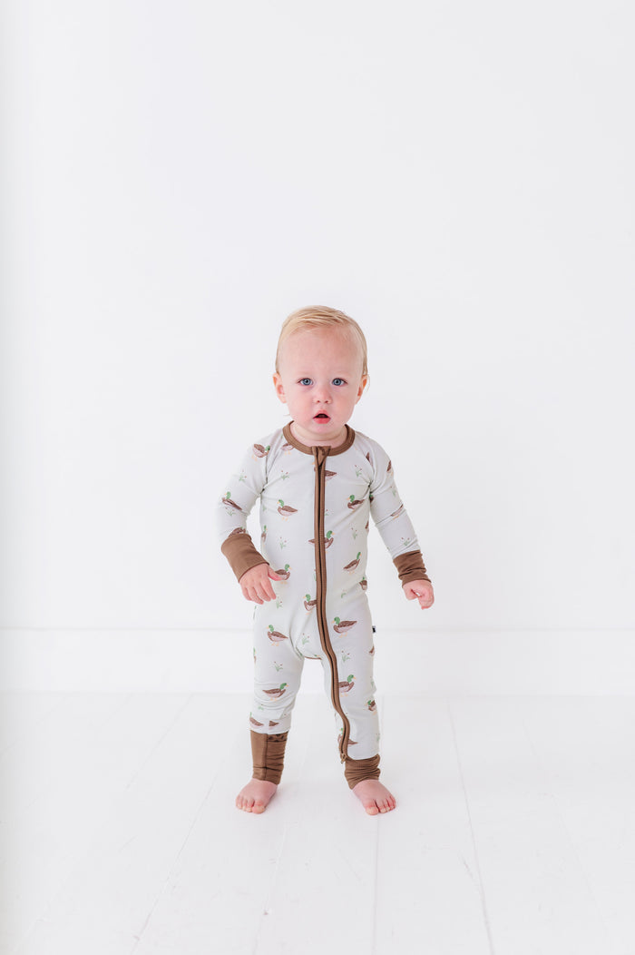 Baby wearing a white onesie with brown accents on a white background